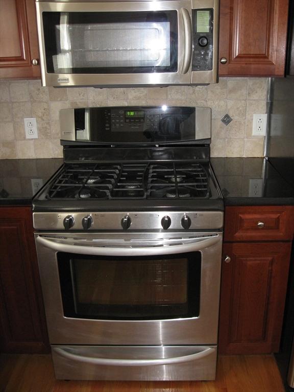 kitchen featuring light wood-type flooring, dark countertops, stainless steel appliances, and decorative backsplash