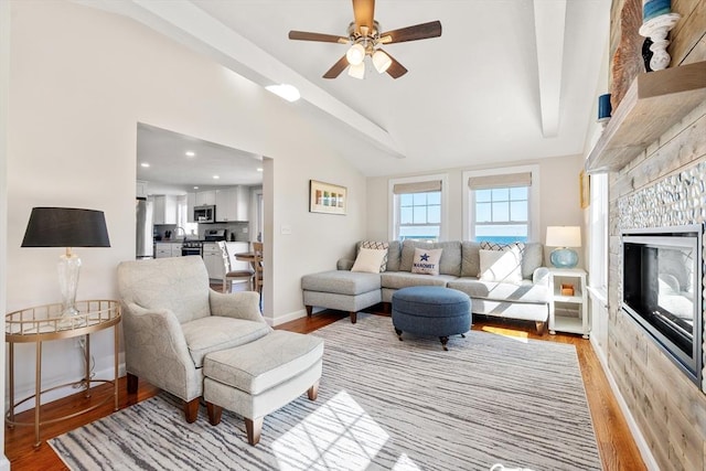 living area featuring a ceiling fan, vaulted ceiling, light wood-style flooring, and baseboards