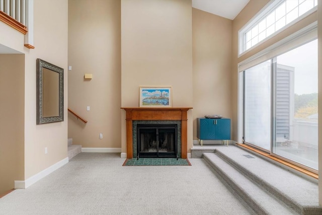 living room featuring a fireplace with flush hearth, carpet flooring, a towering ceiling, stairs, and baseboards