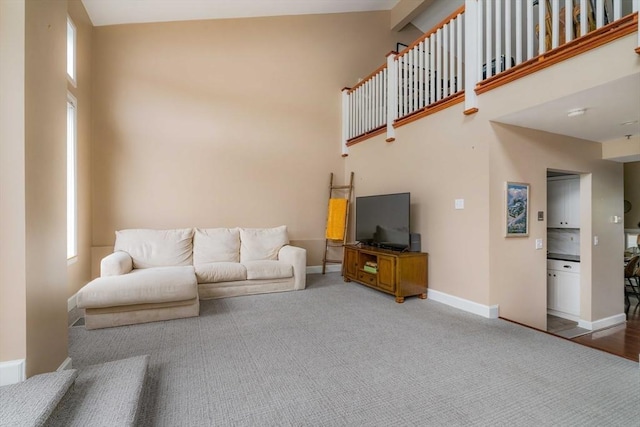 living room featuring carpet floors, a wealth of natural light, a towering ceiling, and baseboards