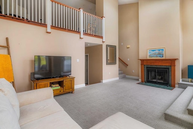 living room featuring carpet floors, a towering ceiling, stairway, a fireplace with flush hearth, and baseboards