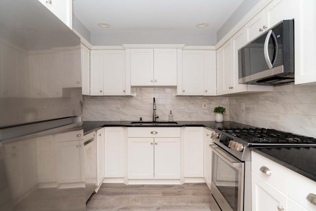 kitchen with appliances with stainless steel finishes, backsplash, a sink, and white cabinets