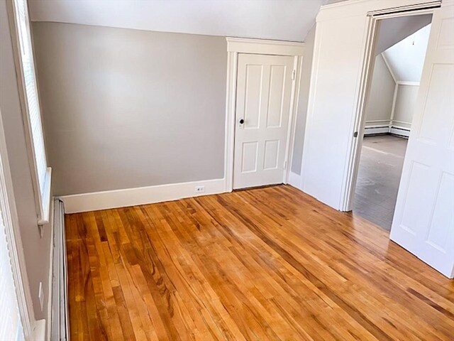 spare room with light wood-style floors, lofted ceiling, a baseboard heating unit, and baseboards