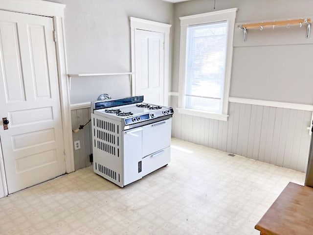kitchen with white gas range oven, a wainscoted wall, plenty of natural light, and light floors