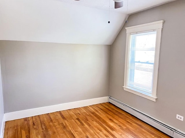 additional living space featuring a baseboard heating unit, a ceiling fan, vaulted ceiling, baseboards, and light wood-type flooring