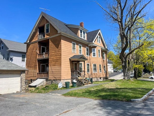 view of side of home featuring a chimney, a garage, a balcony, a lawn, and asphalt driveway