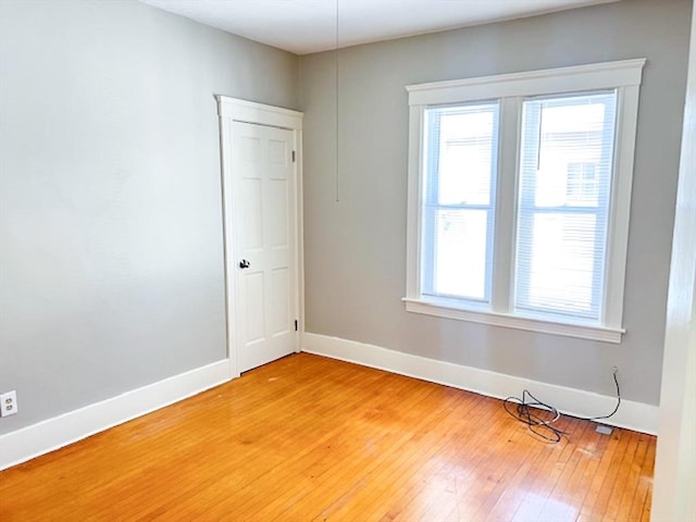 empty room with healthy amount of natural light, baseboards, and light wood finished floors