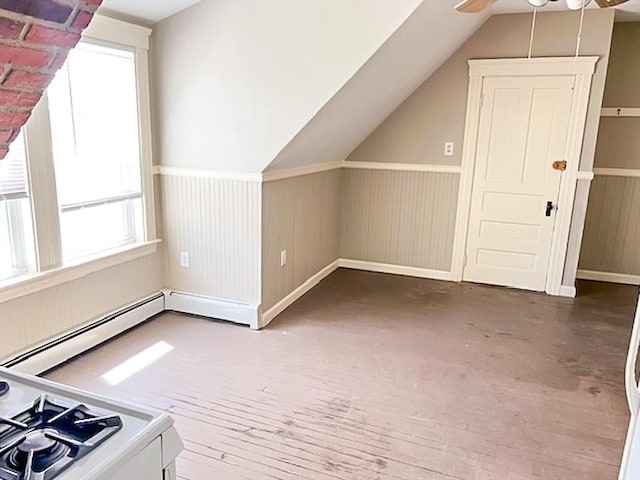 bonus room featuring a ceiling fan, vaulted ceiling, a baseboard heating unit, a wainscoted wall, and wood finished floors