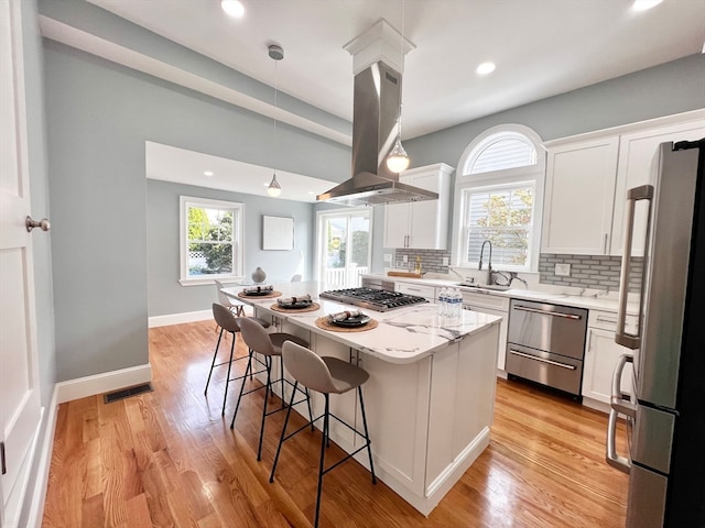 kitchen featuring appliances with stainless steel finishes, island range hood, plenty of natural light, and hanging light fixtures