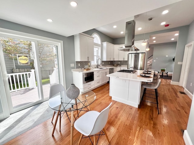 kitchen featuring pendant lighting, a center island, sink, island range hood, and white cabinetry