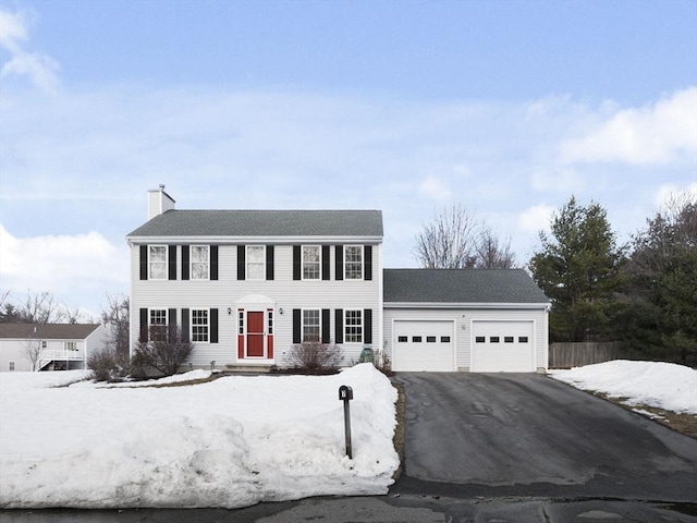 colonial-style house with aphalt driveway, a chimney, and an attached garage