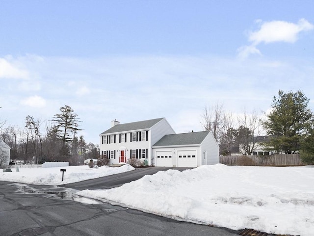 colonial home with an attached garage, a chimney, and fence