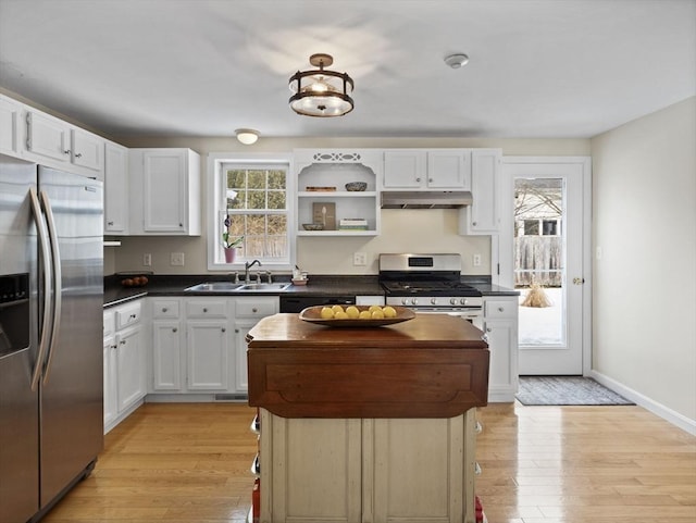 kitchen with dark countertops, under cabinet range hood, appliances with stainless steel finishes, and a sink