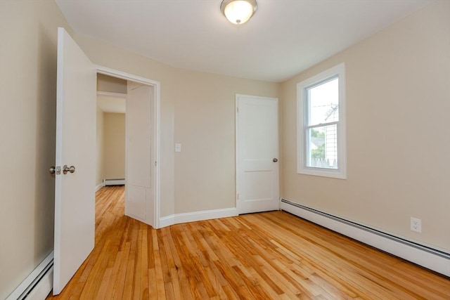 unfurnished bedroom with baseboard heating, light wood-type flooring, and baseboards