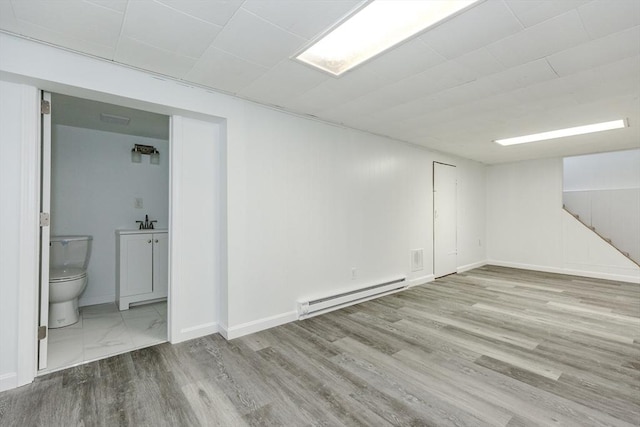 finished below grade area with baseboard heating, wood finished floors, a sink, and baseboards