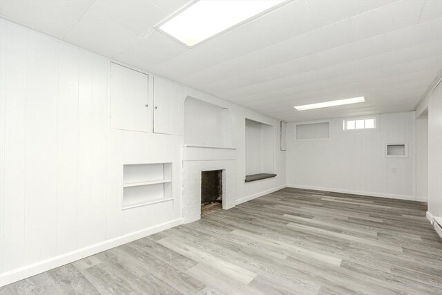 unfurnished living room featuring wood finished floors, a brick fireplace, built in shelves, and baseboards