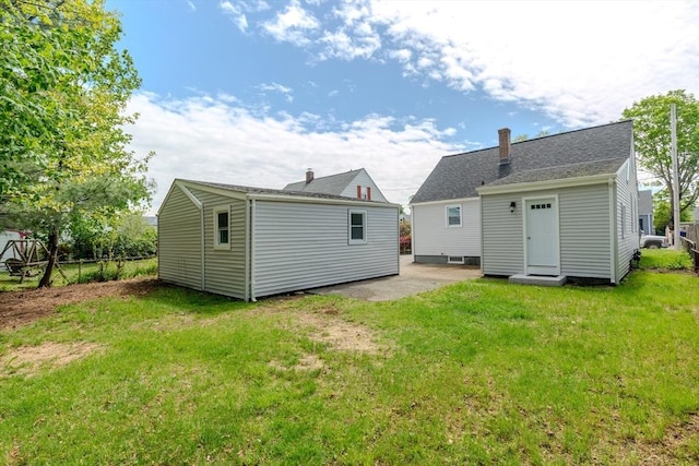 back of property featuring a lawn, a patio, and an outbuilding