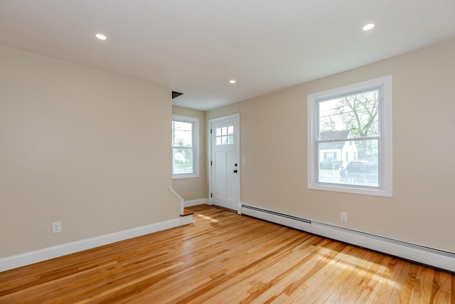 empty room with a baseboard radiator, light wood-style flooring, baseboards, and recessed lighting