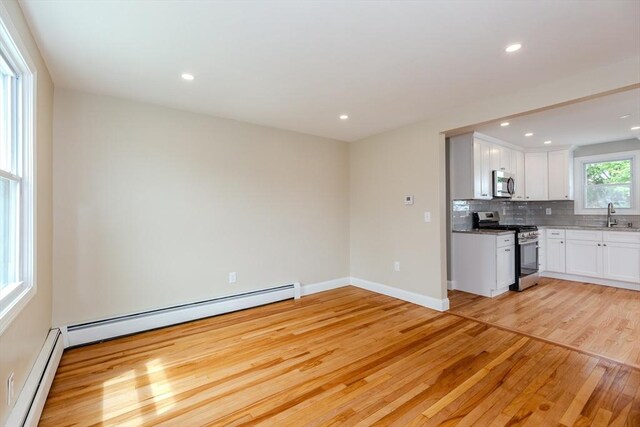 unfurnished living room featuring light wood finished floors, a baseboard heating unit, recessed lighting, baseboards, and a sink