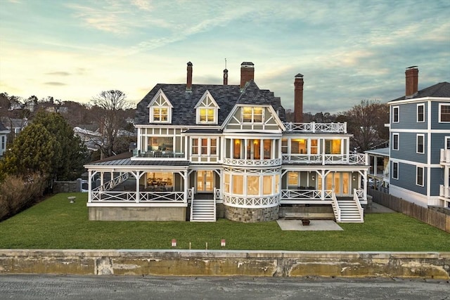 back house at dusk featuring a balcony and a lawn