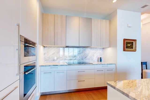 kitchen with light stone countertops, light hardwood / wood-style floors, light brown cabinets, black electric cooktop, and tasteful backsplash