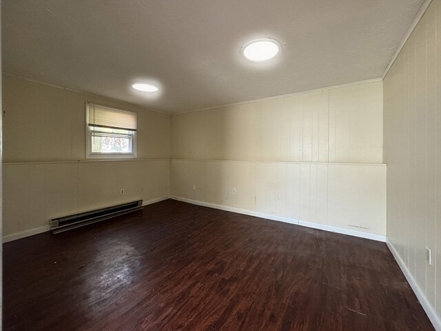 spare room with dark hardwood / wood-style flooring, a baseboard radiator, and wood walls