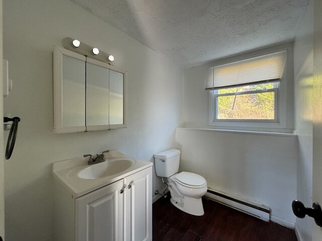 bathroom featuring vanity, a textured ceiling, a baseboard heating unit, wood-type flooring, and toilet