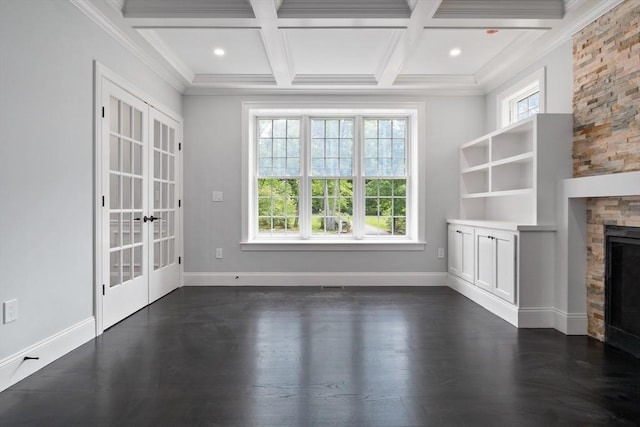 unfurnished living room with coffered ceiling, french doors, a stone fireplace, crown molding, and beamed ceiling