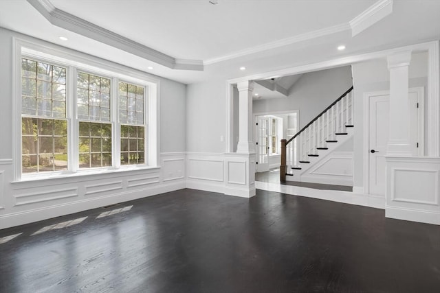 empty room featuring ornamental molding, a tray ceiling, ornate columns, and dark wood-type flooring