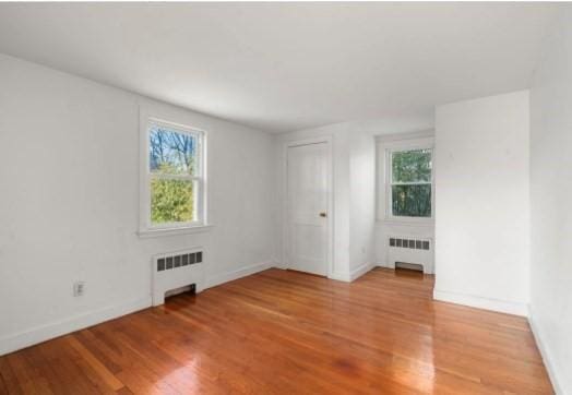 empty room with light hardwood / wood-style floors, radiator, and a wealth of natural light