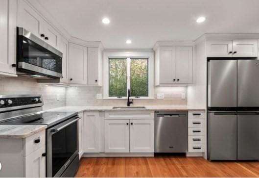 kitchen featuring white cabinets, appliances with stainless steel finishes, light hardwood / wood-style floors, and sink