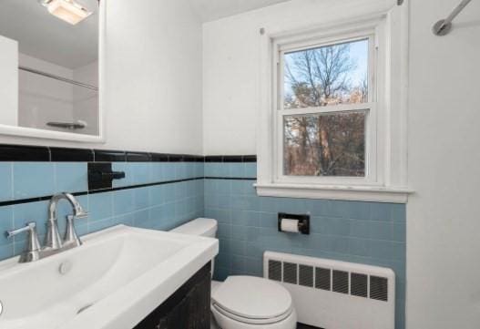 bathroom featuring tile walls, toilet, vanity, and radiator heating unit