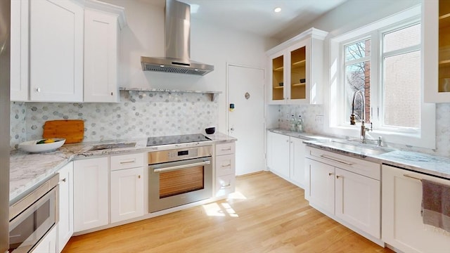 kitchen featuring light wood-style flooring, a sink, stainless steel appliances, exhaust hood, and glass insert cabinets