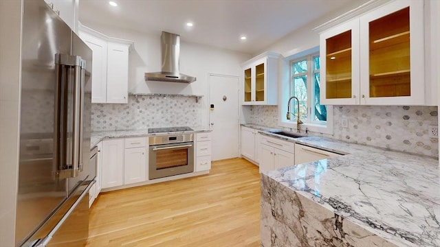 kitchen featuring light stone countertops, a sink, stainless steel appliances, light wood-style floors, and wall chimney exhaust hood