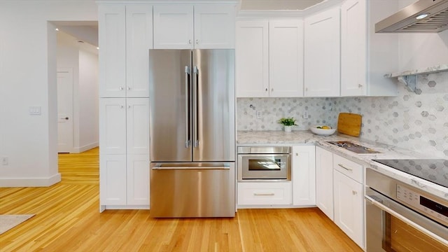 kitchen with light wood-style flooring, appliances with stainless steel finishes, wall chimney exhaust hood, and white cabinetry