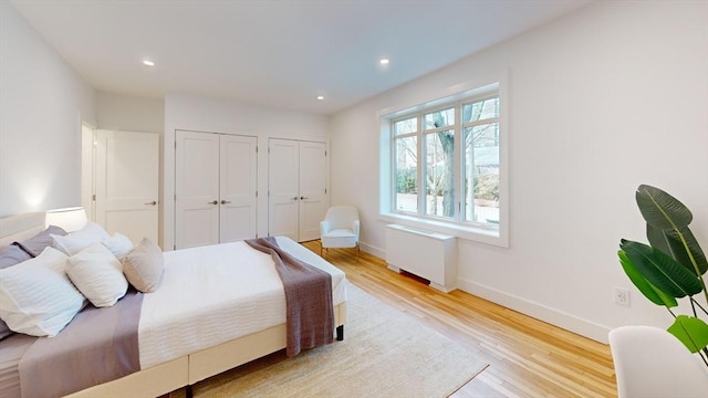 bedroom with baseboards, multiple closets, light wood-type flooring, radiator heating unit, and recessed lighting