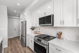 260 Elm St Unit 302, Everett, MA 02149 - kitchen featuring stainless steel appliances, white cabinets, light countertops, light wood finished floors, and backsplash
