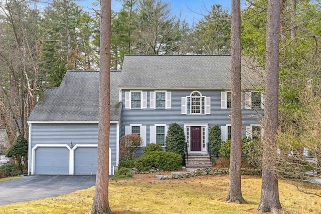 view of front facade with aphalt driveway, a garage, roof with shingles, and a front lawn