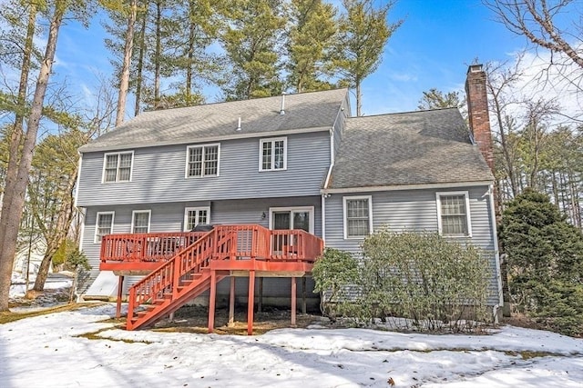 snow covered property featuring stairway, a chimney, a deck, and a shingled roof