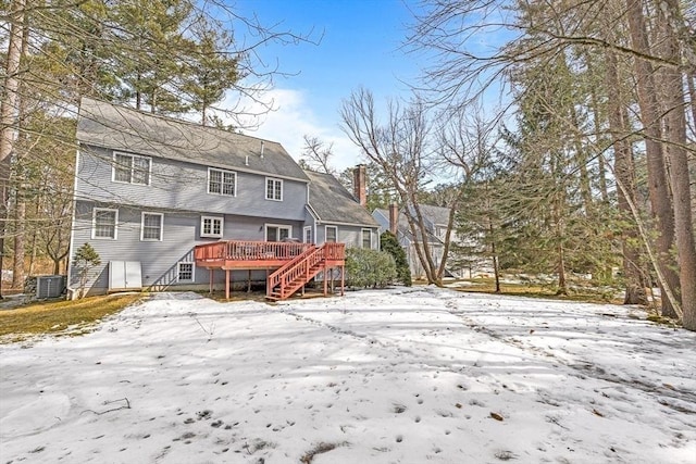 snow covered back of property featuring central air condition unit, a deck, and a chimney