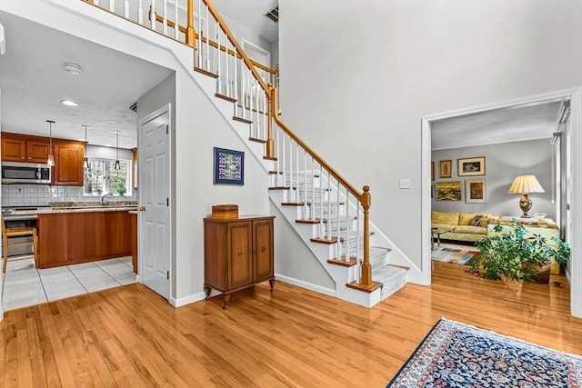 staircase with visible vents, a high ceiling, baseboards, and wood finished floors