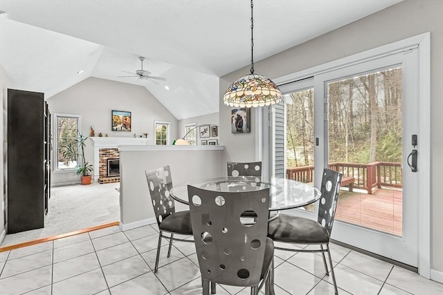 dining room with light tile patterned floors, a healthy amount of sunlight, a brick fireplace, and vaulted ceiling