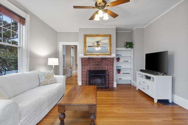 living area with ceiling fan, a brick fireplace, light wood-style floors, and ornamental molding