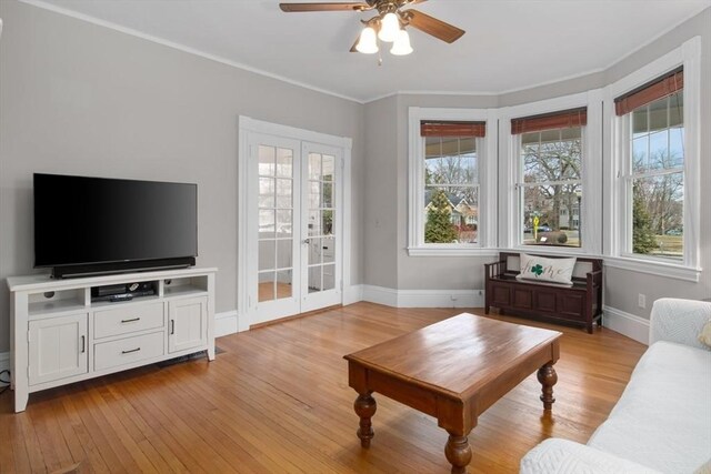 living room featuring ceiling fan, baseboards, crown molding, and light wood-style floors