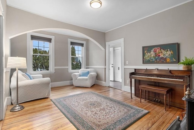 sitting room featuring baseboards, arched walkways, hardwood / wood-style floors, and crown molding