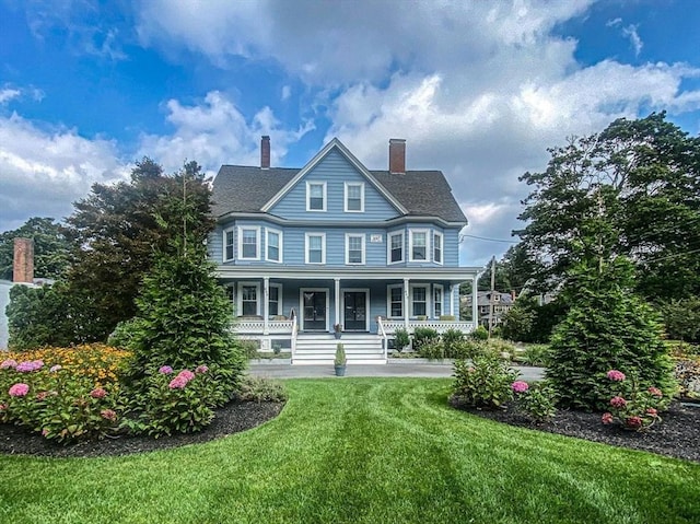 view of front facade with covered porch, a chimney, a front yard, and a shingled roof