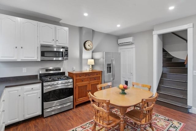 kitchen featuring dark wood-type flooring, an AC wall unit, dark countertops, stainless steel appliances, and white cabinets