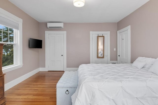 bedroom featuring light wood-type flooring, baseboards, and a wall mounted AC