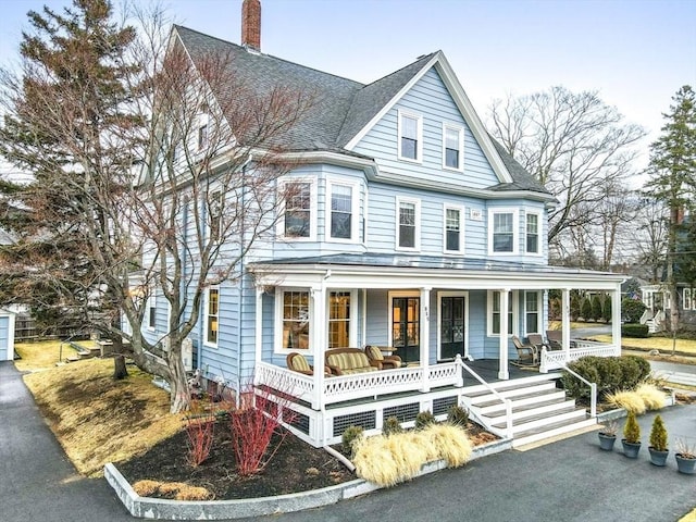 view of front of property with a shingled roof, a porch, and a chimney