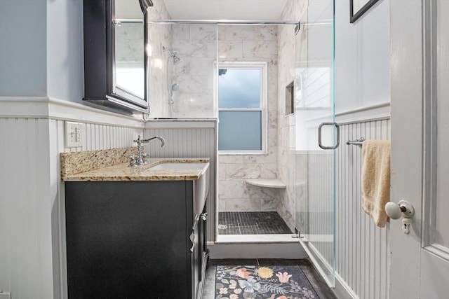 full bathroom featuring vanity, a wainscoted wall, and a stall shower